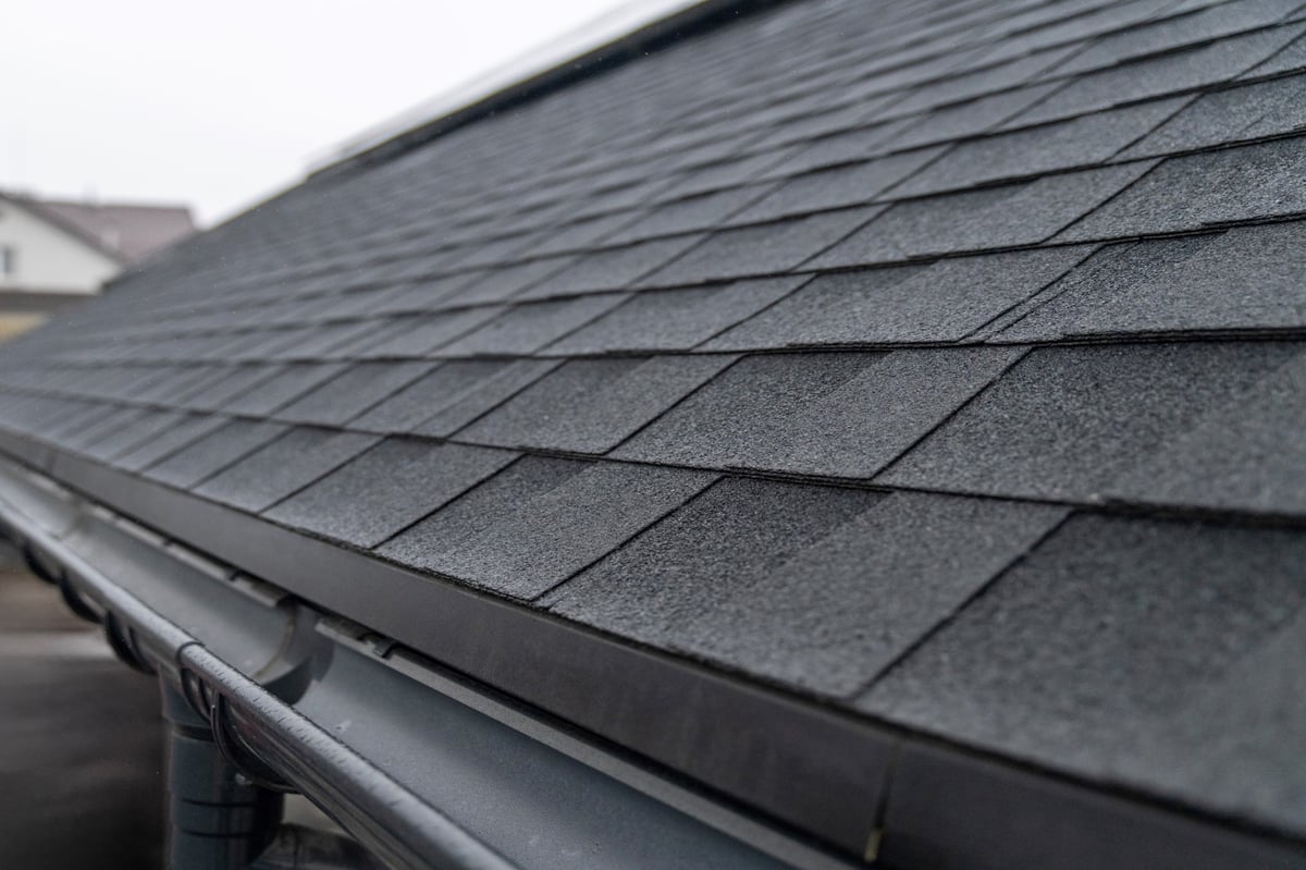 Dark gray asphalt roof shingles with rain gutter system close up